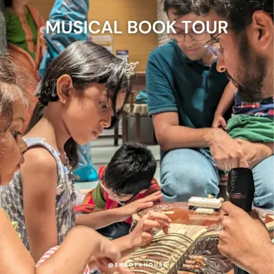 A group of children intently focused on learning the intricacies of a musical instrument from a patient artist. This is the core of our Wonderful Vaadya Project: close, hands-on interaction.