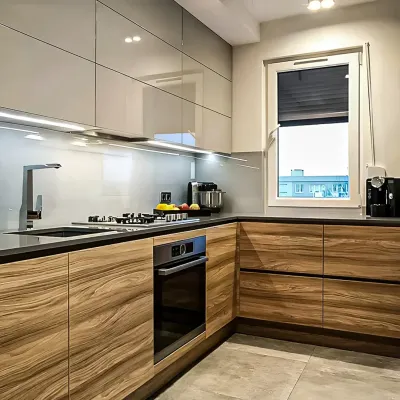 A sleek L-shaped kitchen combining high-gloss grey upper cabinets with warm wood-grain lower cabinets. We installed under-cabinet LED lighting to illuminate the black granite countertop and ensure a well-lit workspace.