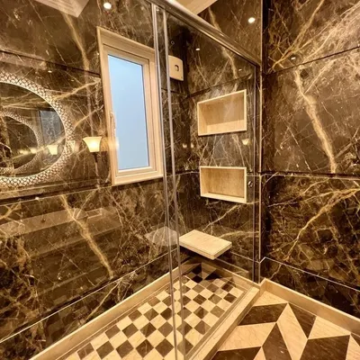 This bathroom at C-257 is a masterclass in luxury. It features floor-to-ceiling dark marble, a glass-enclosed shower with a built-in seat, and a unique geometric-patterned floor.