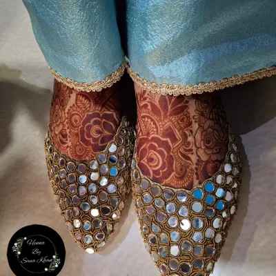 Your bridal look is complete with beautifully adorned feet. This design peeks out elegantly from a pair of traditional mirror-work juttis.