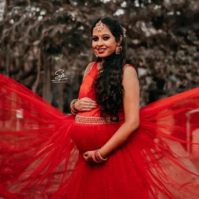 A close-up portrait of a radiant mom-to-be. The vibrant red dress and traditional jewelry create a stunning contrast with the natural background, resulting in a powerful and beautiful maternity photograph.
