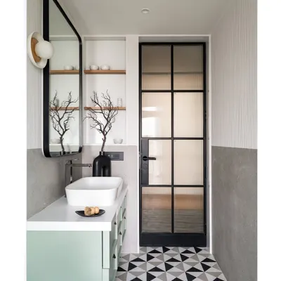 This master bath features a subtle interplay of nexion stone tiles and white fluted accents. The design is complemented by a mint green vanity with a pristine white marble countertop and a sleek black metal-framed mirror.