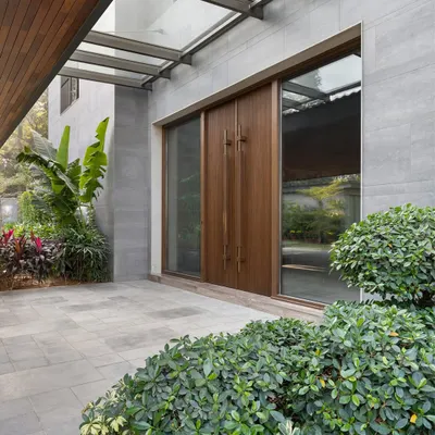 The main entrance of the K Residence, featuring large teak doors by Artius Glulam set within a stone-clad facade. The design of the entrance porch creates a welcoming transition from the lush landscaping to the home's interior.