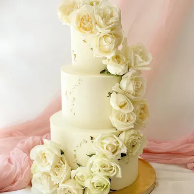An absolutely stunning three-tier wedding cake covered in a cascading waterfall of fresh white roses. The simple, elegant design is enhanced with subtle gold leaf flecks for a touch of luxury.