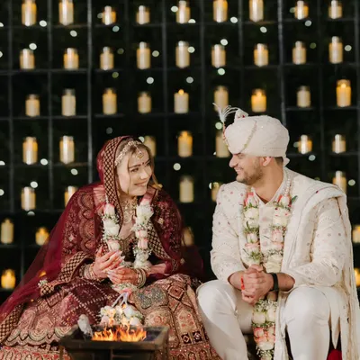 By the sacred fire, against a wall of candles, the couple shares a quiet moment during their pheras. This is where promises are made and forever begins.
