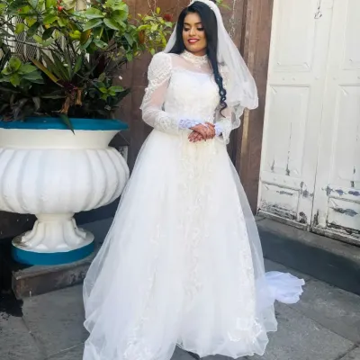 A full-length view of our beautiful bride in her rental wedding gown. This design features delicate lace, elegant long sleeves, and a flowing tulle skirt for a timeless and romantic look.