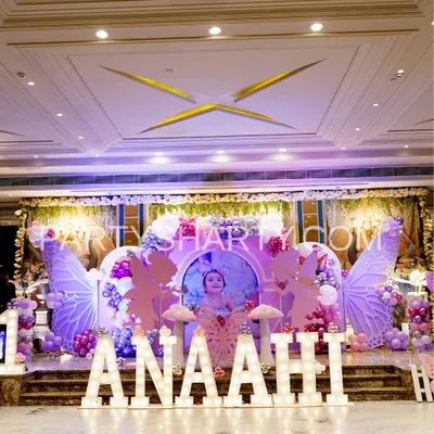A full stage view of a fairy and butterfly-themed birthday, featuring large, illuminated marquee letters spelling the child's name, whimsical fairy wing backdrops, and pastel balloon arrangements.