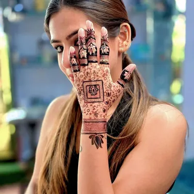 A happy client showing her modern, elegant mehandi. The design features a central square motif with delicate patterns and beautiful lotus designs on the fingers and wrist.