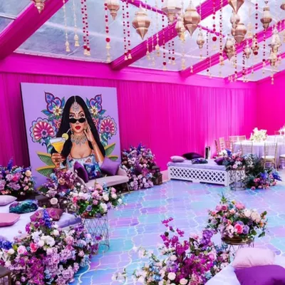 A wide view of a vibrant and funky pop-art Mehendi setup. The entire space is transformed with bright pink drapes, an iridescent floor, and low floor seating with plenty of colorful cushions.