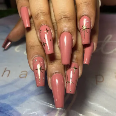 A classy and elegant set of long, coffin-shaped nails in a dusty rose color, adorned with delicate, hand-painted gold stars.