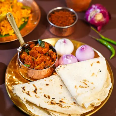 A rustic plate of authentic Maharashtrian Zunka Bhakar, served with raw onions and chili. The simple, earthy styling on a brass plate evokes the feeling of a traditional village meal.