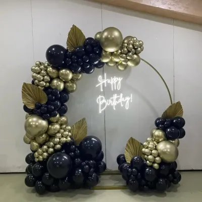 This is a high-end, modern birthday setup featuring a circular frame. The combination of matte black and chrome gold balloons, a custom neon sign, and decorative leaves creates a very sophisticated look.
