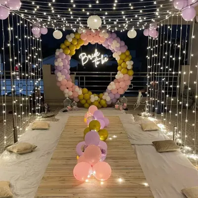 A stunning rooftop dinner party for a "Bride to Be." This setup features a large circular balloon backdrop, a fairy light canopy, and low seating for a magical evening celebrating the bride.