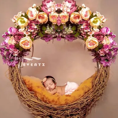 A newborn baby girl sleeps peacefully in a beautiful floral nest prop. This setup uses a rustic twig nest adorned with a halo of pink and cream peonies, creating a delicate and artistic portrait.