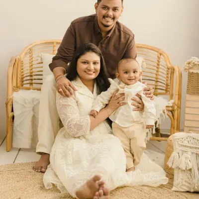 A relaxed and happy family portrait in our signature boho style. The family sits together on a jute rug in front of a rattan bench, creating a warm and inviting scene.