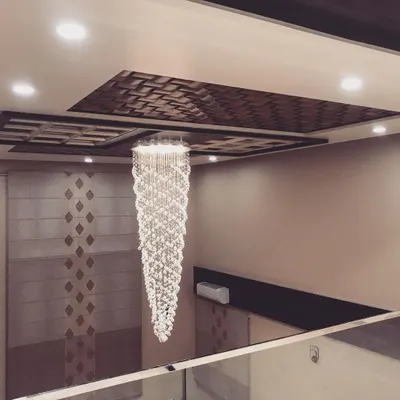 A stunning, multi-tiered crystal chandelier hangs in a double-height space, drawing the eye upward. The ceiling above features a 3D wooden pattern, adding another layer of texture and luxury.