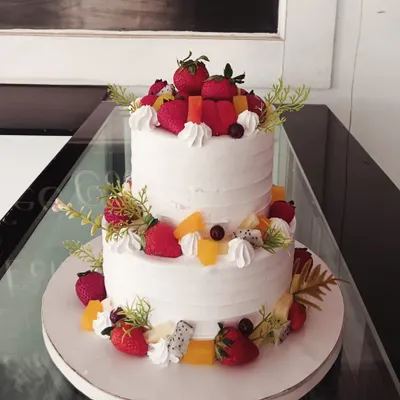 A refreshing two-tiered cake generously decorated with a variety of fresh fruits. This design features whole strawberries, dragon fruit, and orange slices, perfect for a summer celebration.