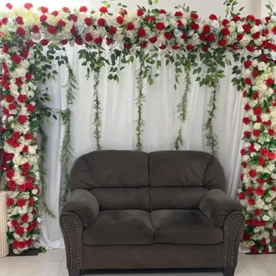 A simple yet beautiful photo corner created in a living room. I built a floral arch using red and white roses with trailing greenery around the client's own sofa, instantly creating a dedicated spot for pictures.