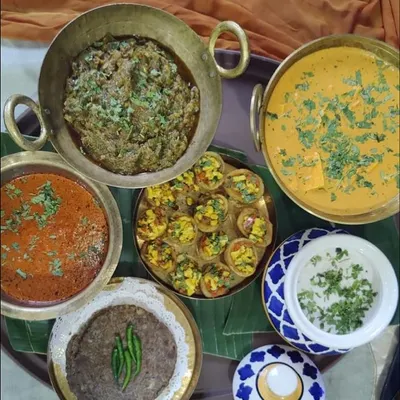 A traditional Indian feast featuring a variety of classic dishes. This spread includes Shahi Paneer, a mixed vegetable dish, raita, and roti, all served in authentic brassware.