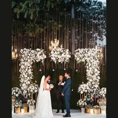 A breathtaking view of an outdoor Catholic wedding ceremony. The couple stands under a magnificent floral arch, exchanging vows in a setting that feels both grand and deeply intimate.