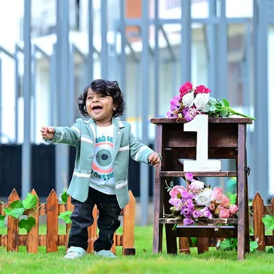 A burst of pure happiness! This outdoor shot captures the joy of turning one, with a simple fence and floral prop that complements the natural background.
