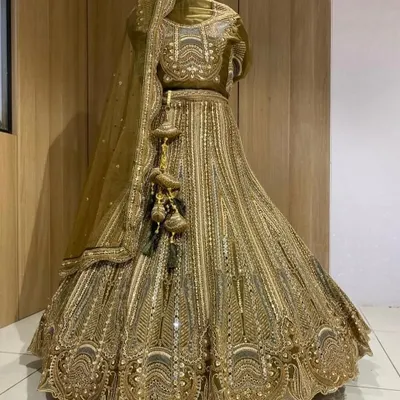 A stunning golden lehenga displayed on a mannequin. This piece is covered in intricate embroidery and sequins, perfect for a bride who wants a glamorous, shimmering look.