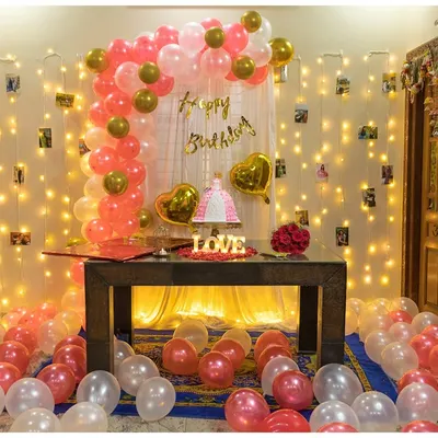 A full view of our popular indoor birthday setup. We combine a pink and gold balloon arch with a curtain of fairy lights and scattered floor balloons to create a fun and photo-ready party zone.