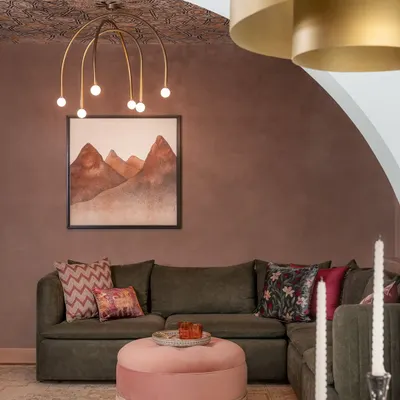 A close-up of the living room in the Quiet Ornate home. We love layering textures and patterns, like the deep rosé tinted walls, the intricate wallpaper on the ceiling, and the mix of cushions on the olive sofa.