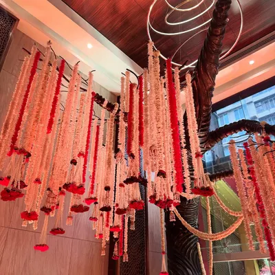 A dramatic ceiling installation featuring a cascade of red and white floral strings hanging from a sculptural tree-like structure, creating a true work of art.