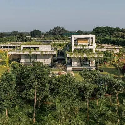 An aerial view of a weekend home where the architecture is completely immersed in a dense, green landscape. The design features green roofs and cascading plants that soften the concrete structure, making it one with its surroundings.