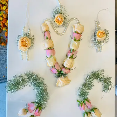 A closer look at a full floral jewelry set laid out before packaging. This design combines soft peach and pink roses with baby's breath and pearls. You can see the full set here: a rose bud necklace, a central maang tikka, matching earrings, and two hathphool hand harnesses.