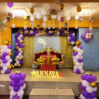 This was for a grand first birthday celebration in a party hall. I decorated the entire stage with a purple, white, and gold theme, including two large balloon pillars, a backdrop for the throne, and photos of the baby hanging from balloons on the ceiling.
