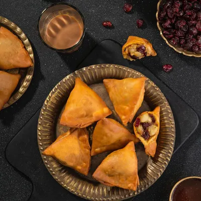 Cranberry-filled samosas, a fusion recipe for US Cranberries India. The dark, moody styling with brass plates and cutting chai glasses gives a rustic yet modern feel.
