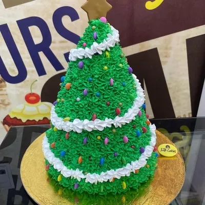 A custom 3kg Christmas tree cake, intricately decorated with green buttercream frosting, colorful sprinkles as lights, and a gingerbread star on top.