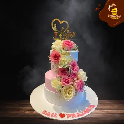 This stunning three-tier engagement cake combines classic white and soft pink, adorned with a spiral of fresh roses. It’s a timeless design that perfectly captures the romance of the occasion for the happy couple.