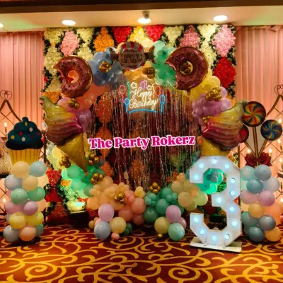 A delicious-looking Candyland theme for a 3rd birthday. I used a flower wall backdrop, a shimmer curtain, and a balloon arch decorated with giant donut, ice cream, and cupcake props.