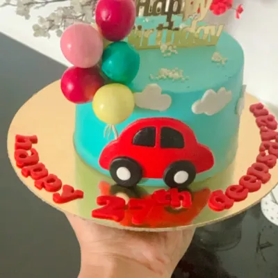 A fun and vibrant birthday cake for a car lover. This bento cake is decorated with a bright red fondant car, fluffy buttercream clouds, and a cluster of balloon toppers, all personalized with the birthday boy's name and age.