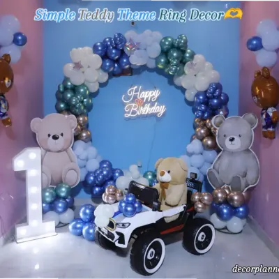 A beary special first birthday! This adorable teddy bear theme features a blue backdrop with a balloon ring, cute teddy bear cutouts, a marquee number '1', and even a teddy driving a toy car. It's a sweet and classic theme for a little one's big day.