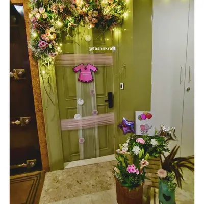 A charming welcome for a baby girl, with a floral arch and fairy lights adorning the front door. The decor includes sweet details like a onesie-shaped balloon and floral baskets, creating a warm and inviting homecoming.