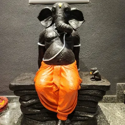 A modern interpretation of Lord Ganesha, sculpted in a relaxed posture. This custom FRP statue features a textured black finish with vibrant orange dhoti, created for a client in Gurgaon.