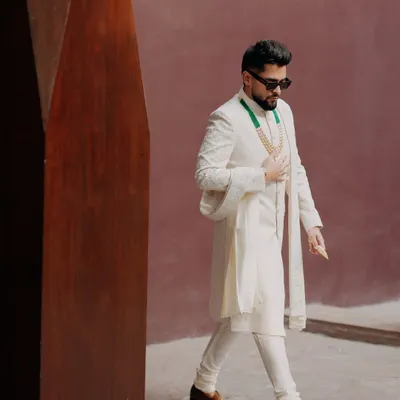 A stylish portrait of the groom, Shrey, looking dapper in his white sherwani and sunglasses. This shot captures his cool confidence and modern style on his wedding day.