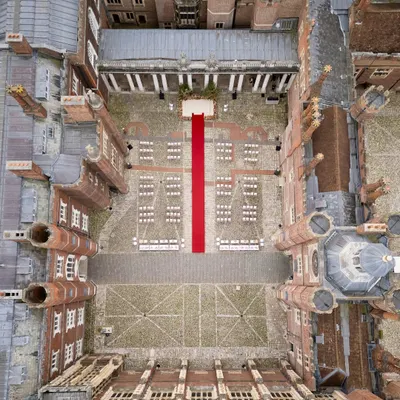A stunning top-down aerial view of the wedding ceremony setup at Hampton Court Palace, UK. This shot showcases the grand scale and precise execution required for events at world-renowned heritage sites.