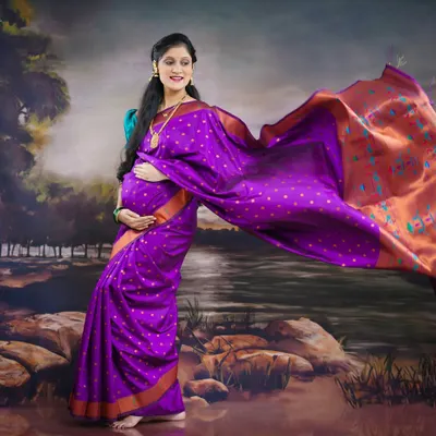 A stunning solo portrait featuring a vibrant purple saree. We create a sense of graceful movement by letting the pallu flow, adding a dynamic and artistic touch to this traditional maternity photo.