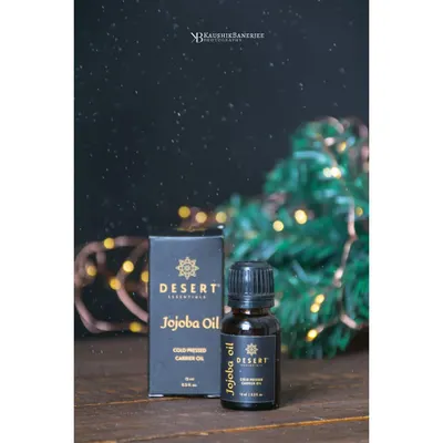 A festive-themed shot for Desert Essentials Jojoba Oil. The dark background with bokeh lights creates a magical, celebratory mood, making the product feel like a special gift.