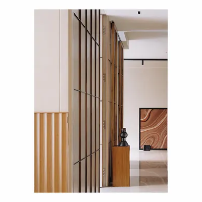 This entire wall is clad in a paneling inspired by Japanese shoji screens, using thin teak wood verticals and black metal batons. It discreetly hides several doors and storage spaces, creating an illusion of connectivity and adding length to the passage.