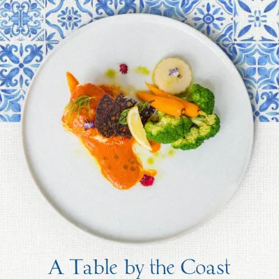 A beautifully plated fish dish with a vibrant orange sauce and fresh vegetables. This plate represents our philosophy of using fresh, seasonal ingredients inspired by the coast.