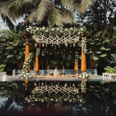 A stunning poolside mandap setup, with traditional wooden pillars and white floral decor beautifully reflected in the water. My team and I transform venues to create breathtaking backdrops for your ceremony.