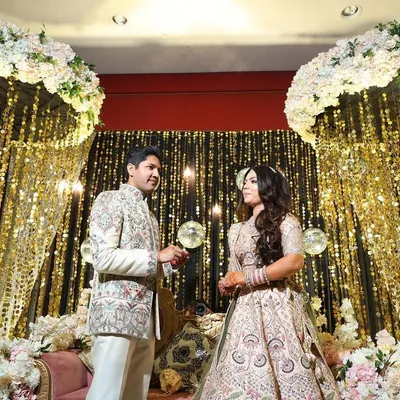 A glamorous engagement stage featuring a backdrop of cascading gold sequins and elegant white floral arches. This design creates a dazzling, celebratory atmosphere perfect for the ring ceremony.