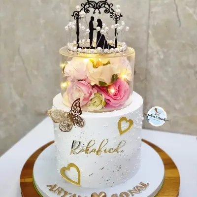 A beautiful two-tier cake for a Roka celebration. The clear spacer tier filled with flowers and fairy lights adds a touch of magic, making it a truly unique centerpiece for the happy couple.