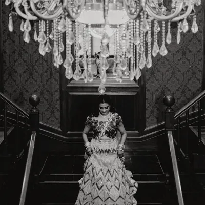 A timeless black and white portrait of the bride on her Sangeet night. The grand chandelier and elegant staircase create a classic, dramatic setting for this beautiful moment of anticipation.